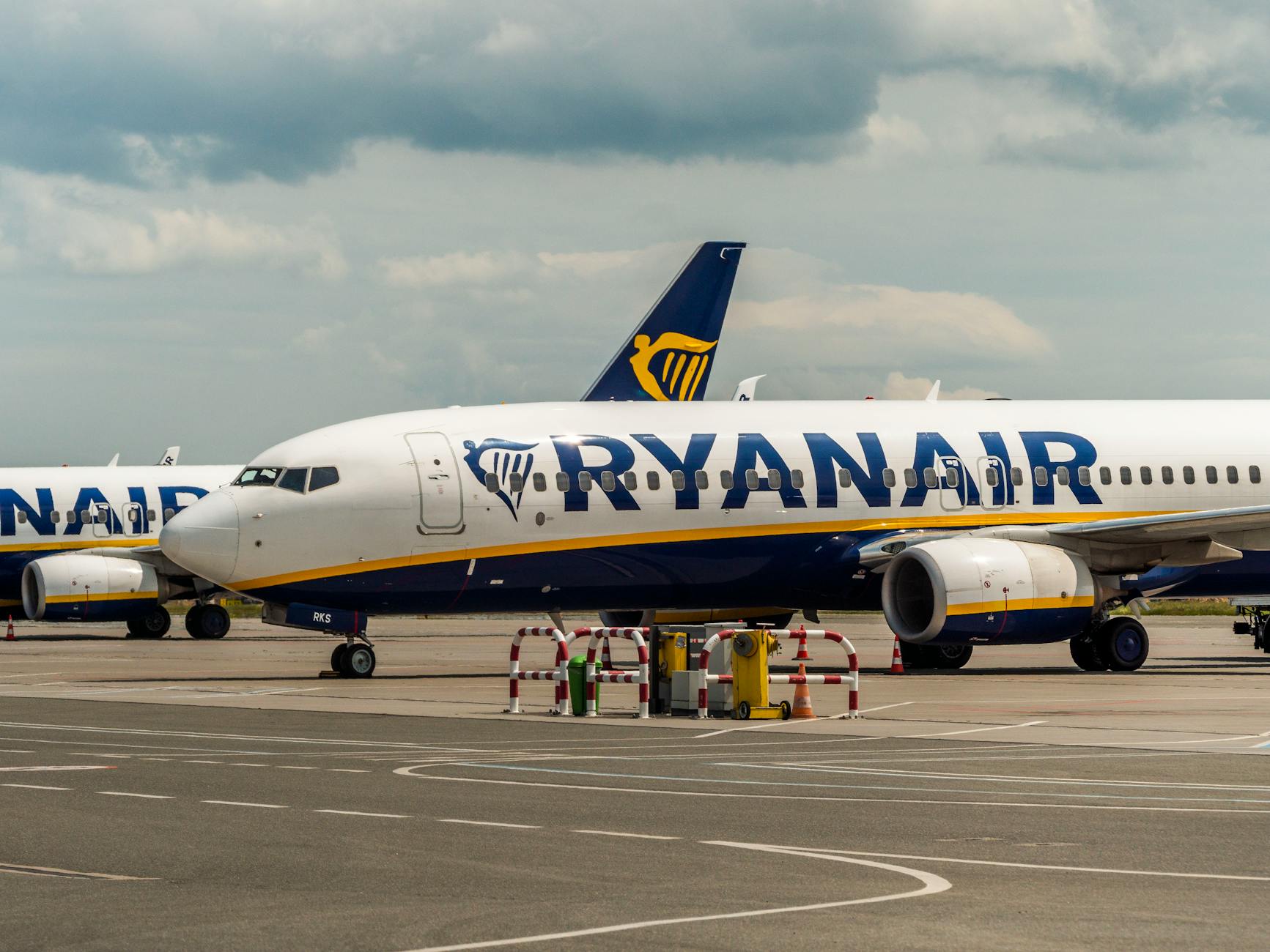 A Ryanair aircraft parked on the airport tarmac during the day under cloudy skies.