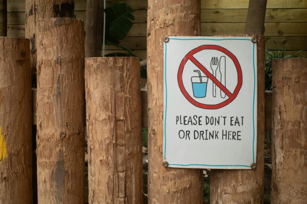 A sign prohibiting eating or drinking attached to wooden logs outdoors.