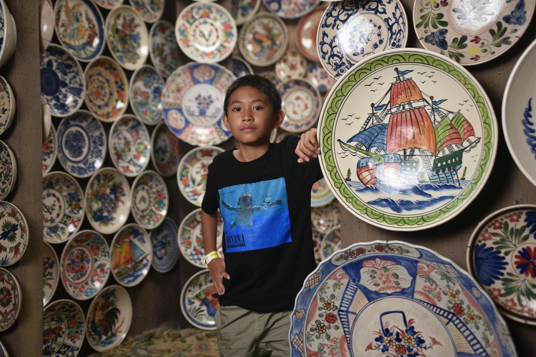 A young boy poses among beautifully painted decorative plates in an artistic gallery setting.