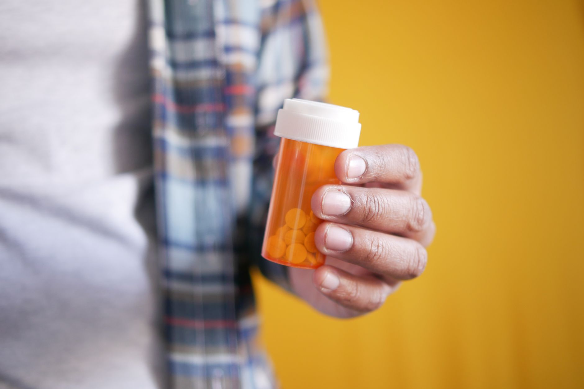 A hand holds a prescription bottle against a bright yellow background, symbolizing healthcare and medication.