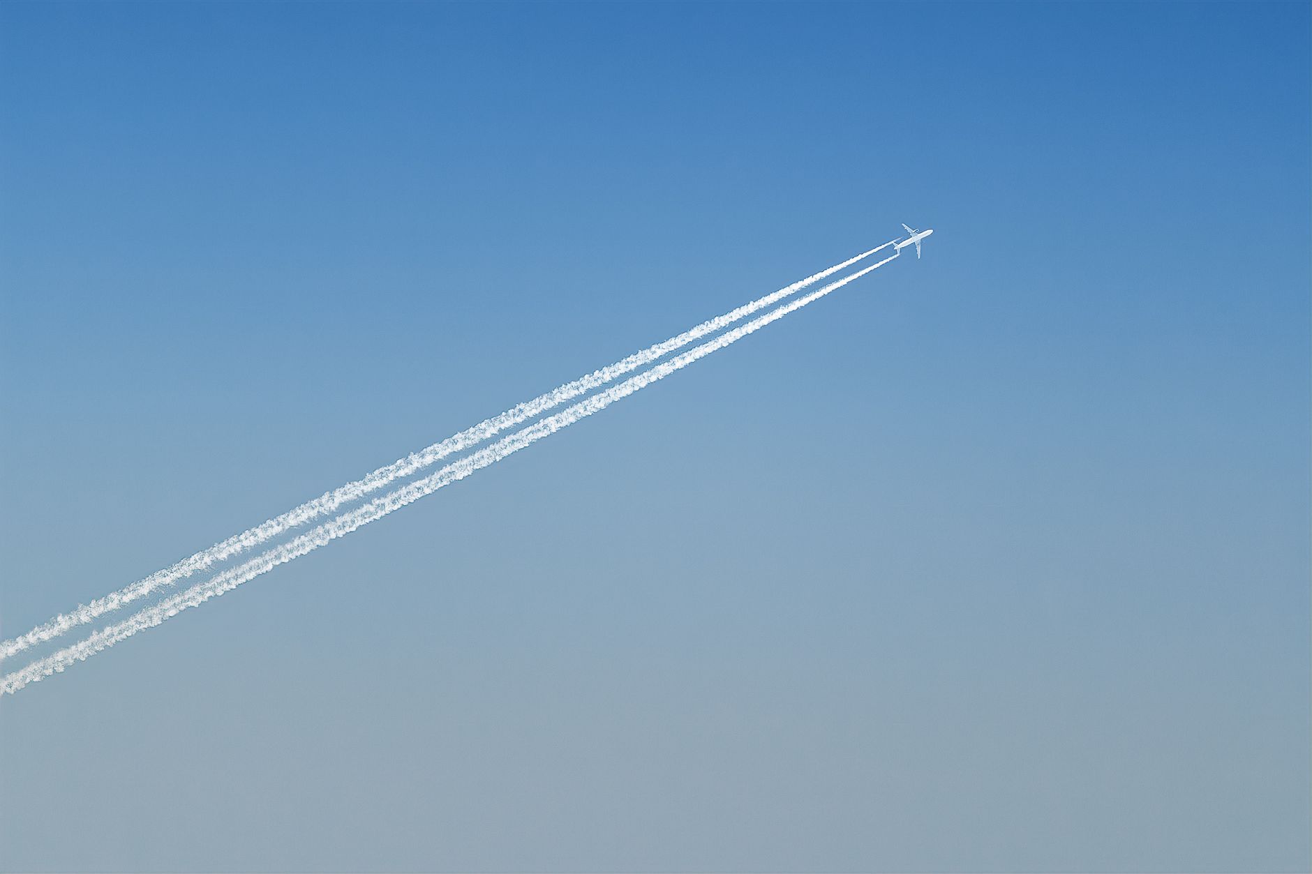 An airplane creating contrails across a clear blue sky, showcasing aviation technology.